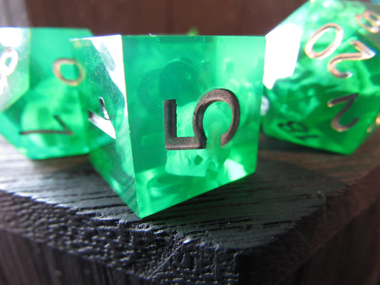 Green polyhedral dice with gold numbers on a dark textured surface gelatinous cube
