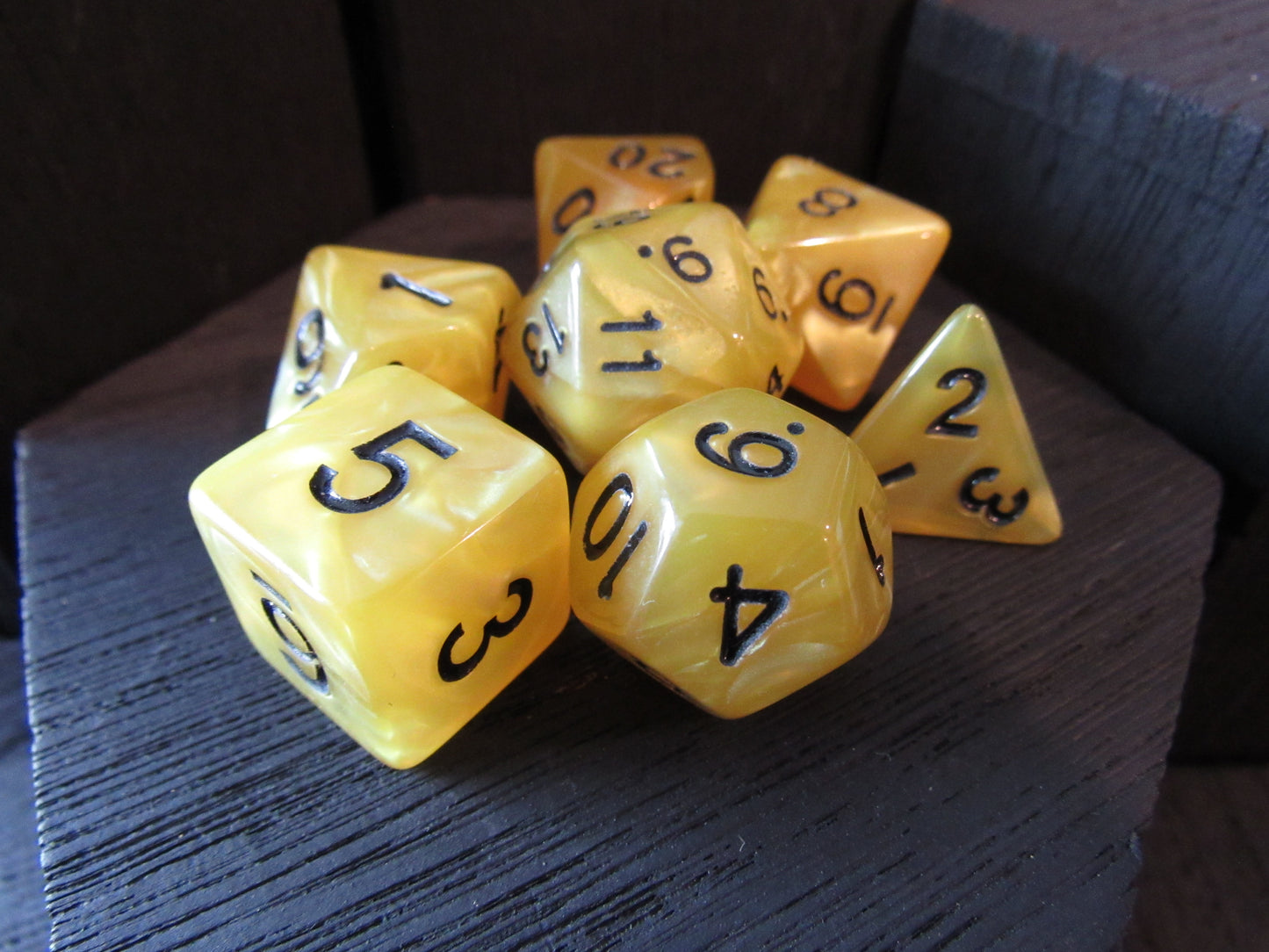 Set of yellow polyhedral dice with black numbers on a dark textured surface