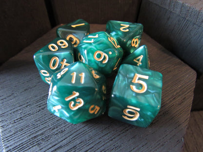 Set of green polyhedral dice with gold numbers on a wooden surface.