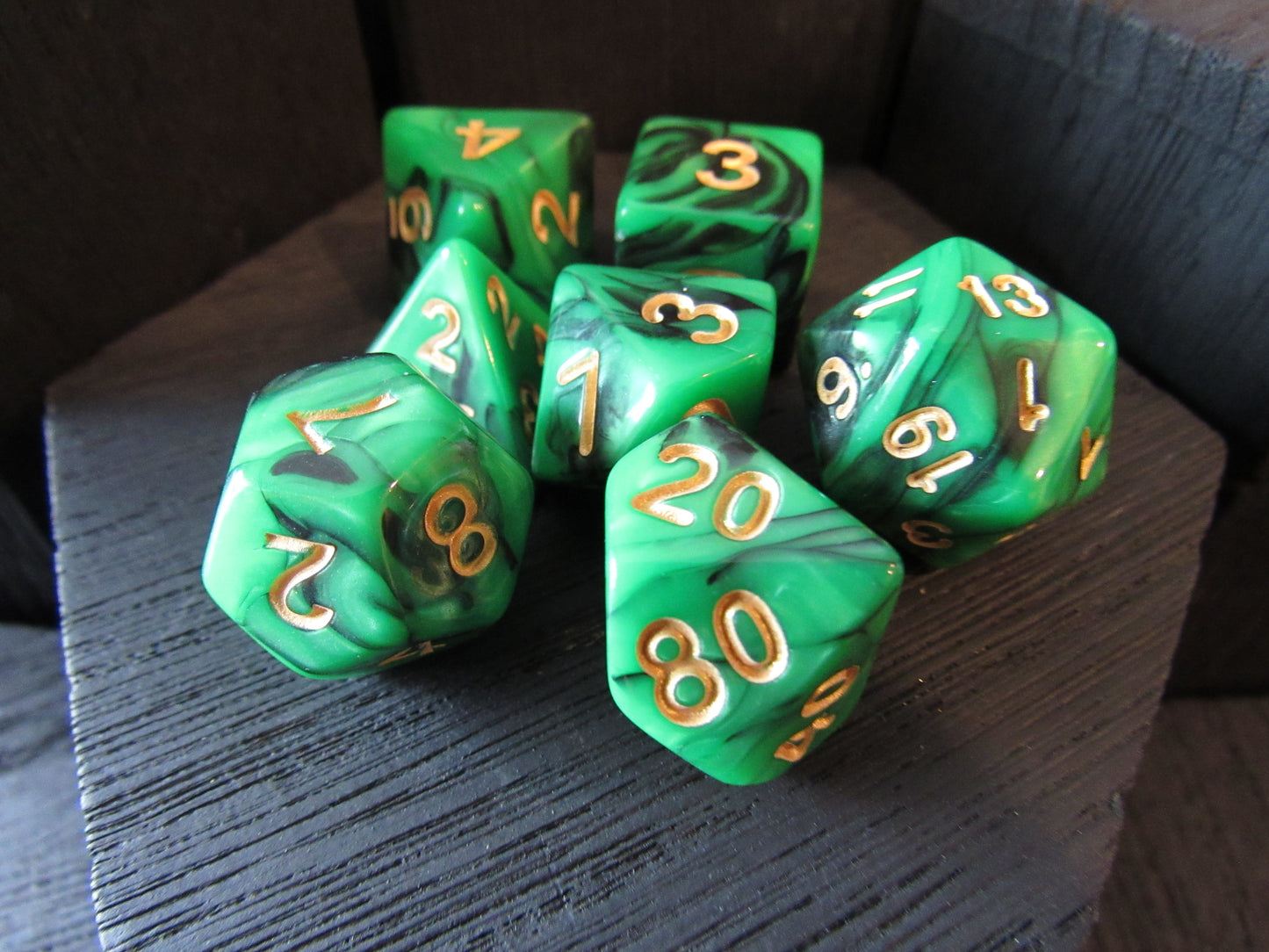 Set of green polyhedral dice with gold numbers on a wooden surface