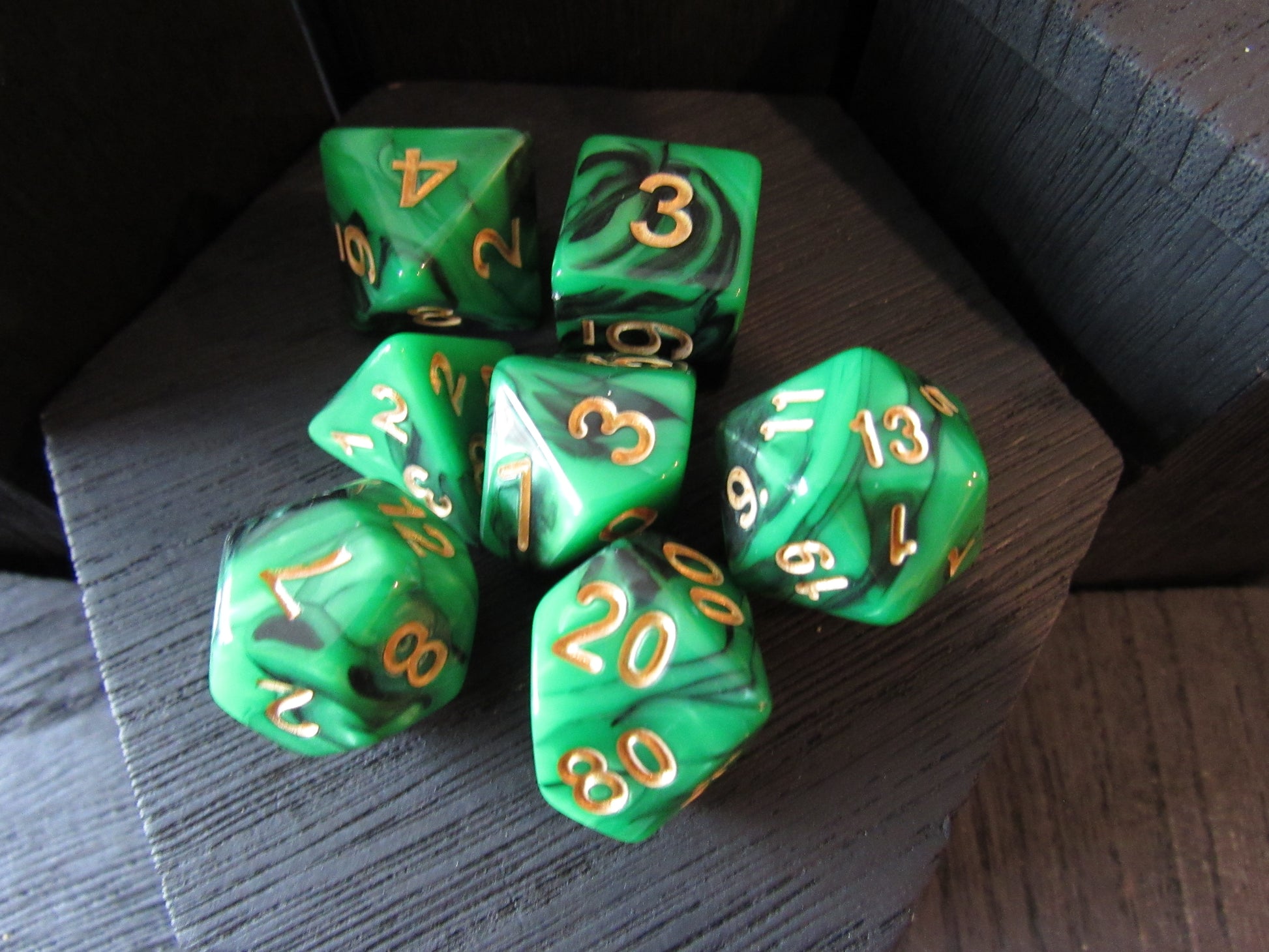 Set of green polyhedral dice with gold numbers on a dark wooden surface