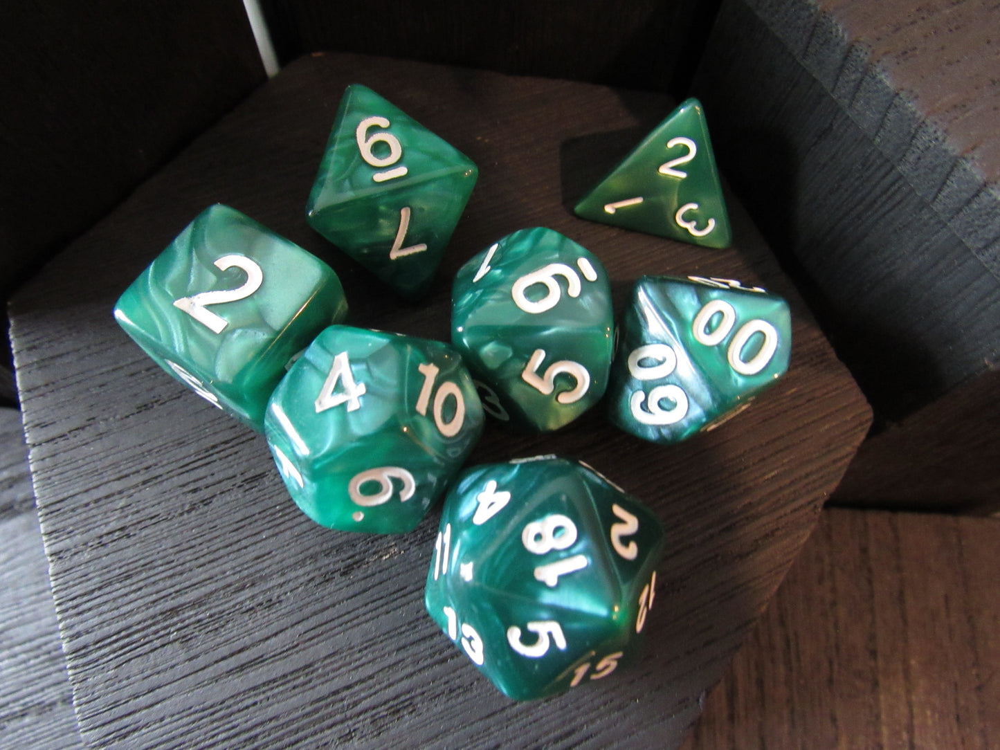 Set of green polyhedral dice with white numbers on a wooden surface