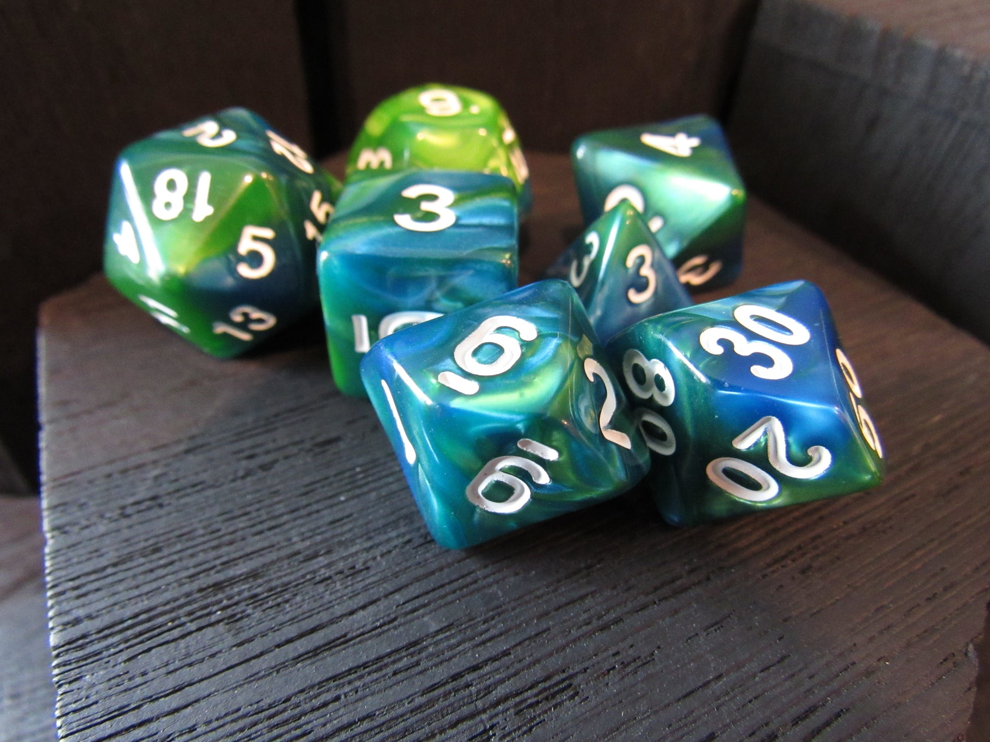 Set of green and blue dice with white numbers on a wooden surface