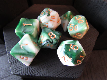 Set of green and white polyhedral dice with orange numbers on a wooden surface