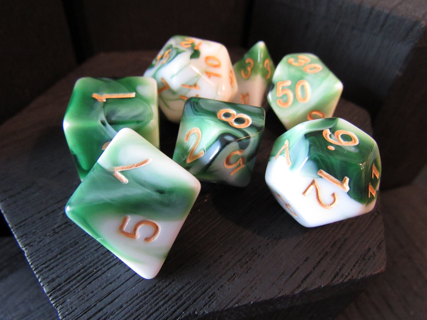 Set of green and white polyhedral dice with orange numbers on a dark surface