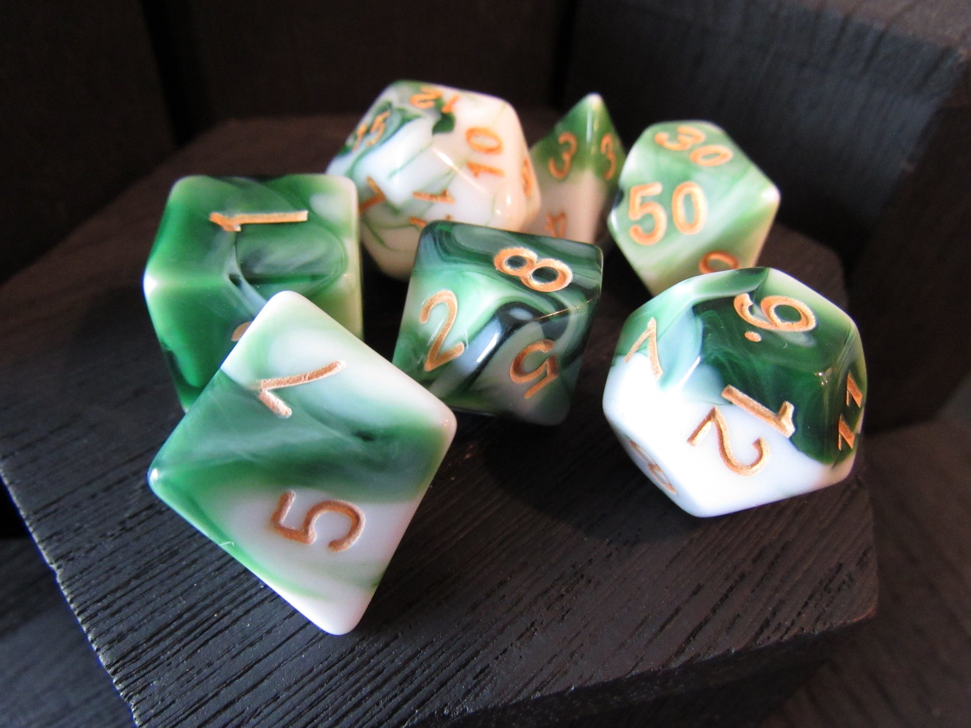Set of green and white polyhedral dice with orange numbers on a dark surface