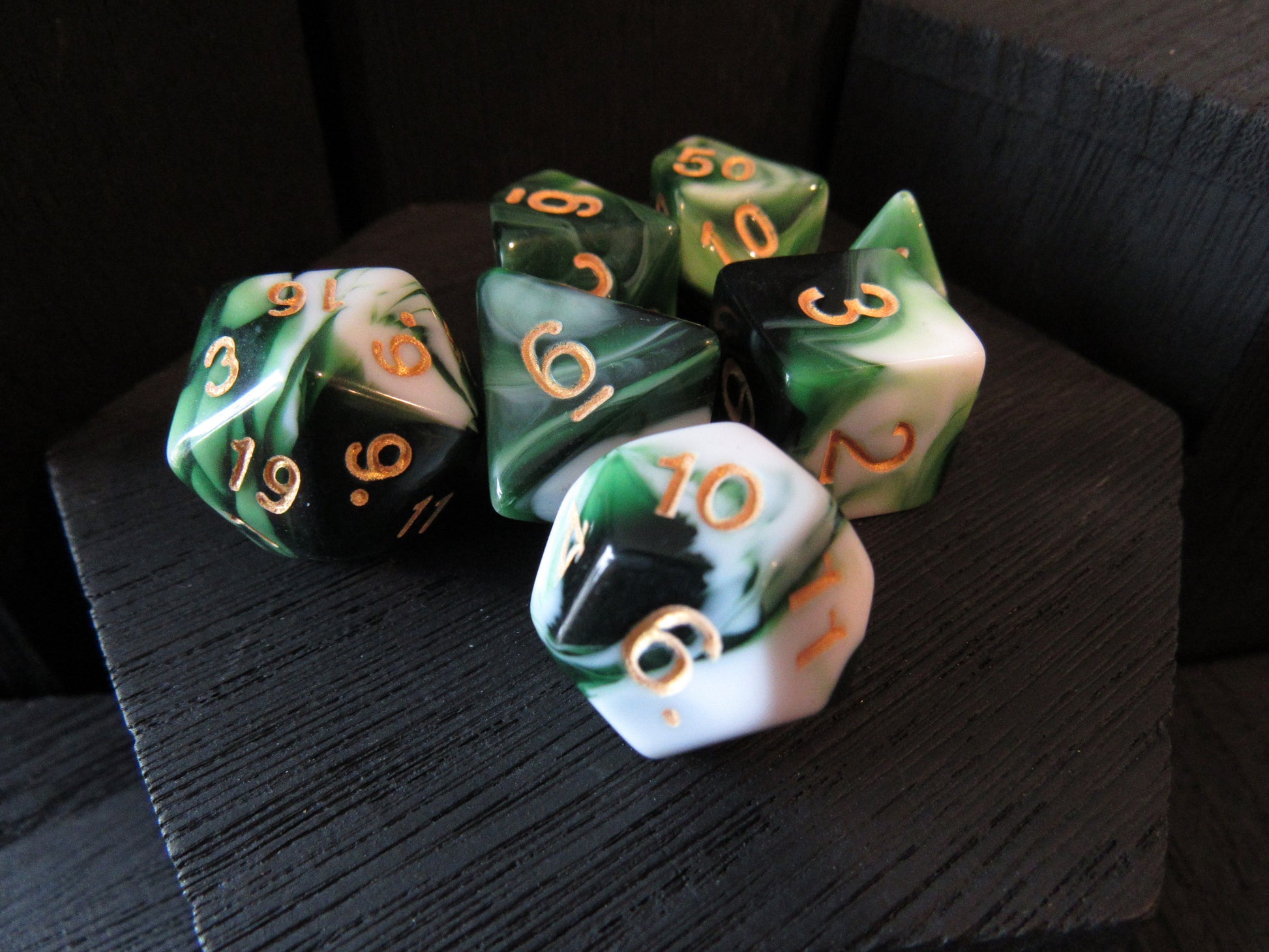 Set of green and white polyhedral dice with gold numbers on a dark surface