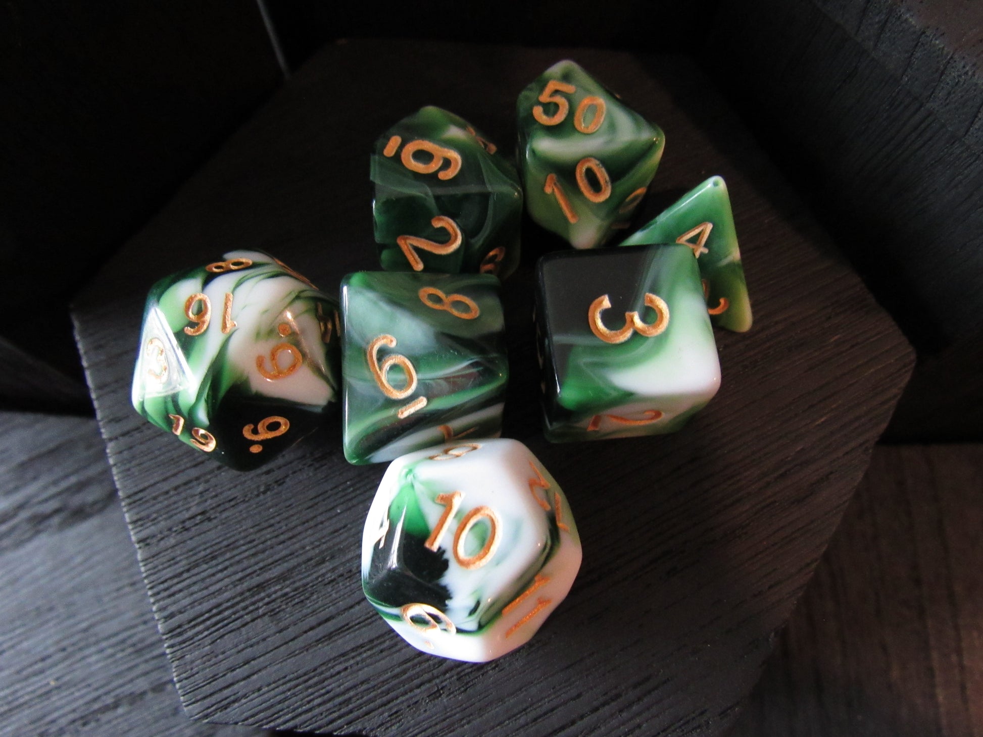 Set of green and black polyhedral dice with gold numbers on a dark surface