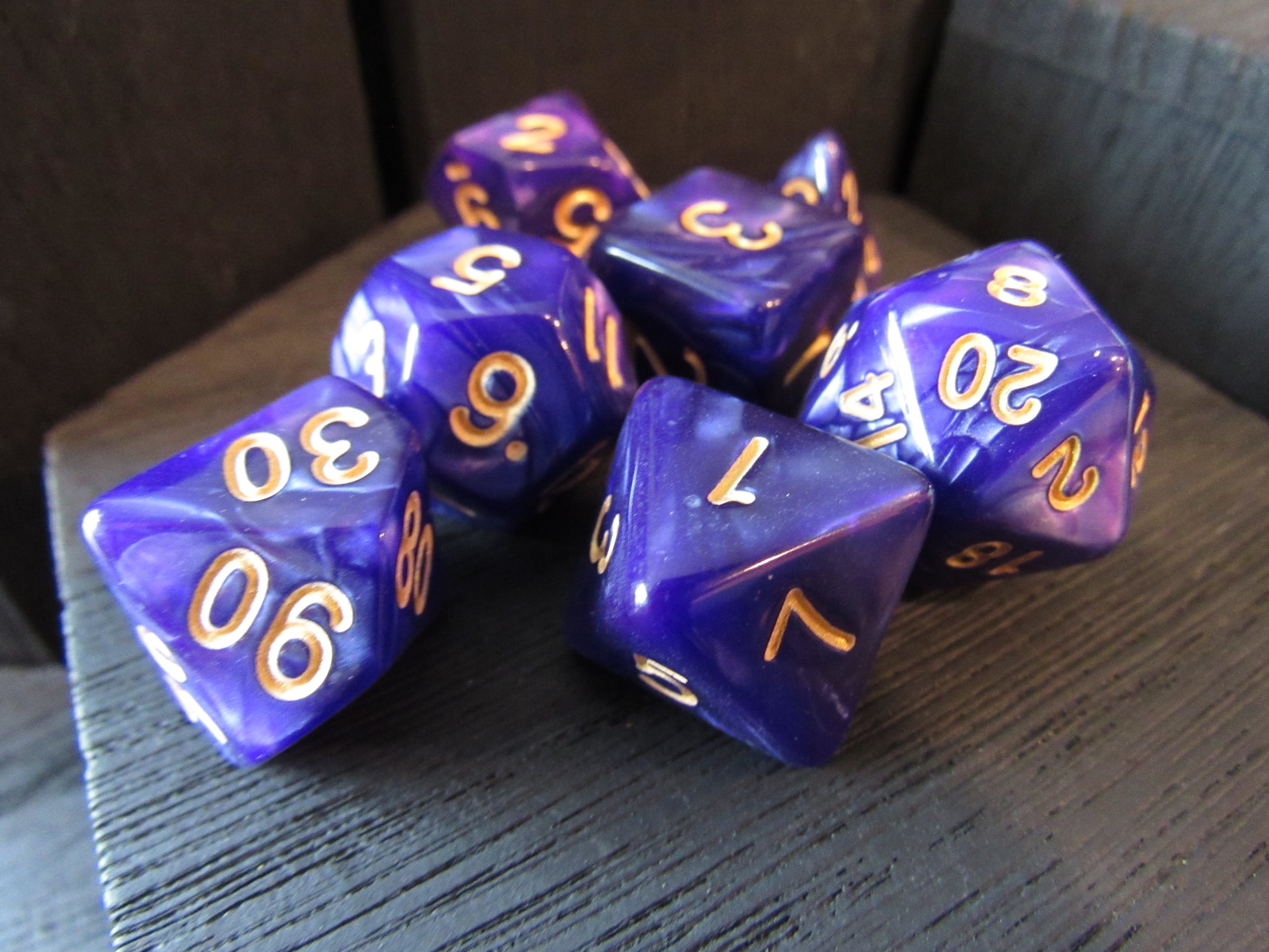 Purple polyhedral dice with gold numbers on a wooden surface
