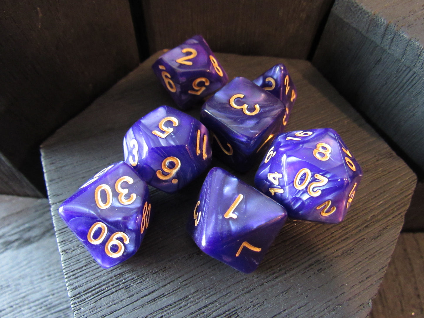Set of purple polyhedral dice with gold numbers on a wooden surface