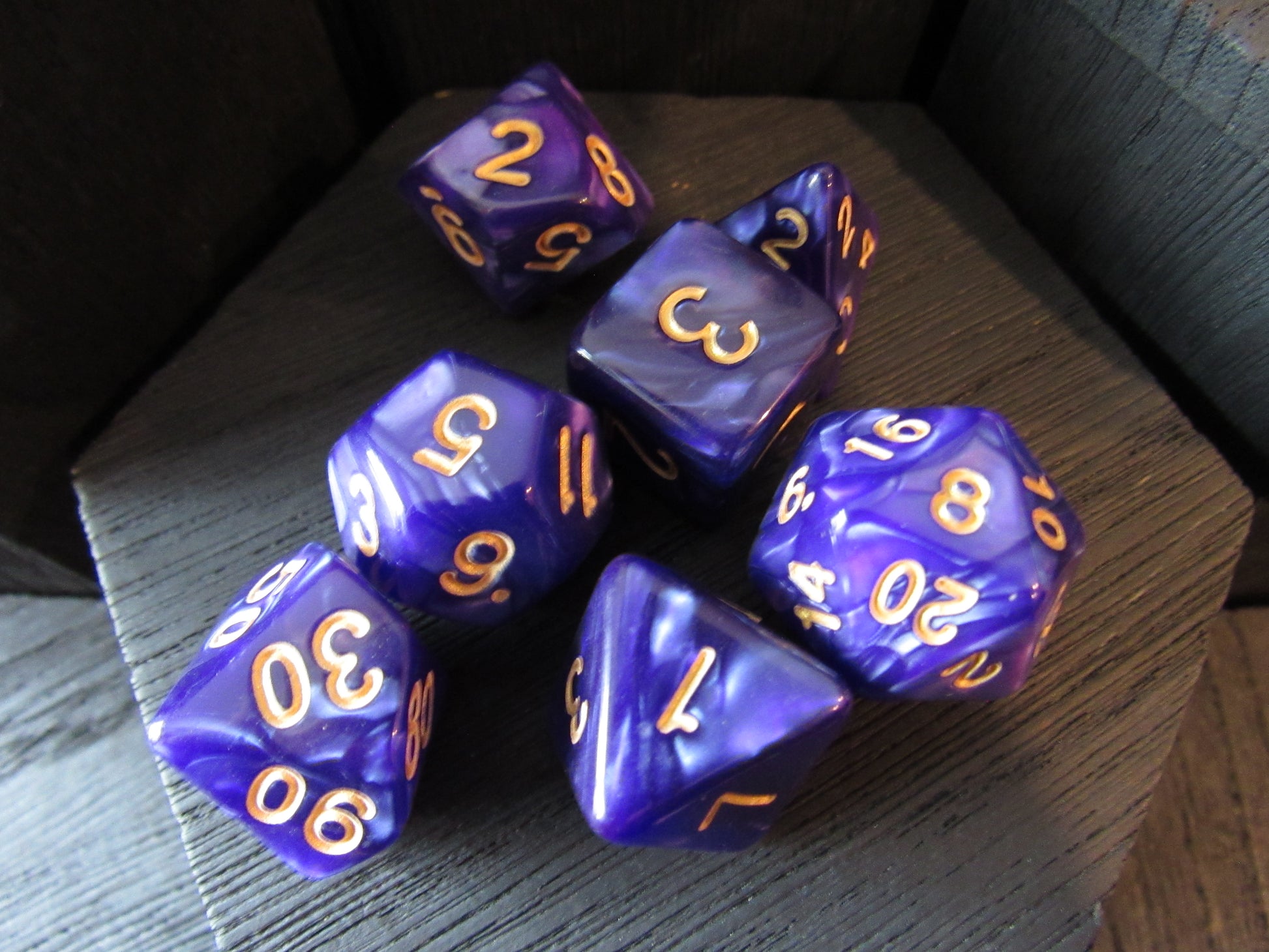 Set of purple polyhedral dice with gold numbers on a wooden surface