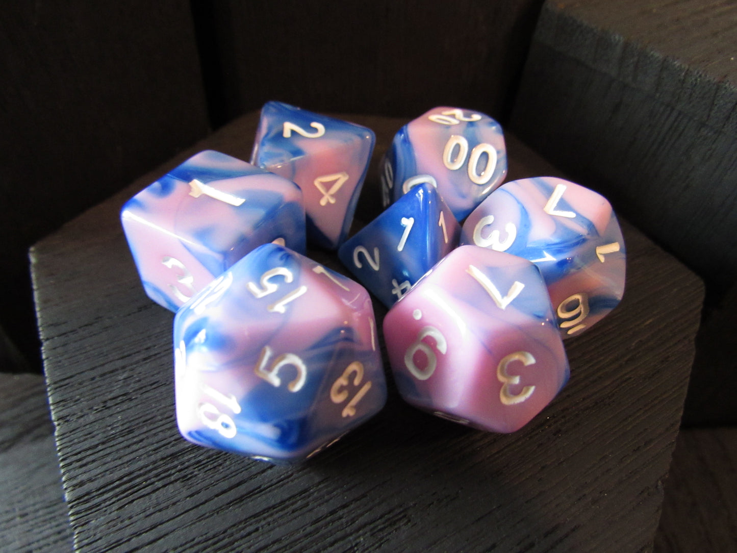 Set of blue and pink marbled dice with gold numbers on a dark surface
