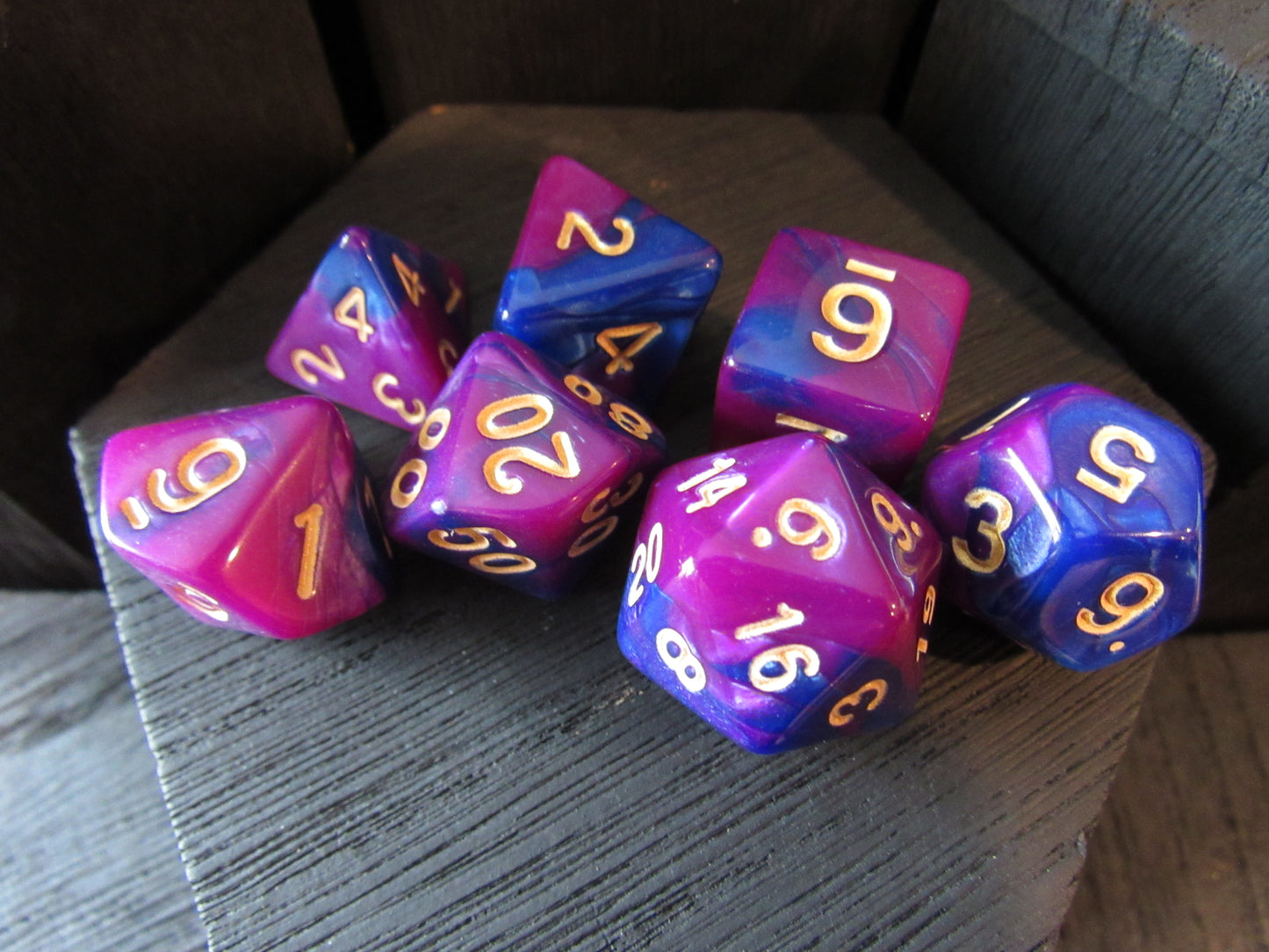 Set of purple and blue polyhedral dice with gold numbers on a wooden surface.