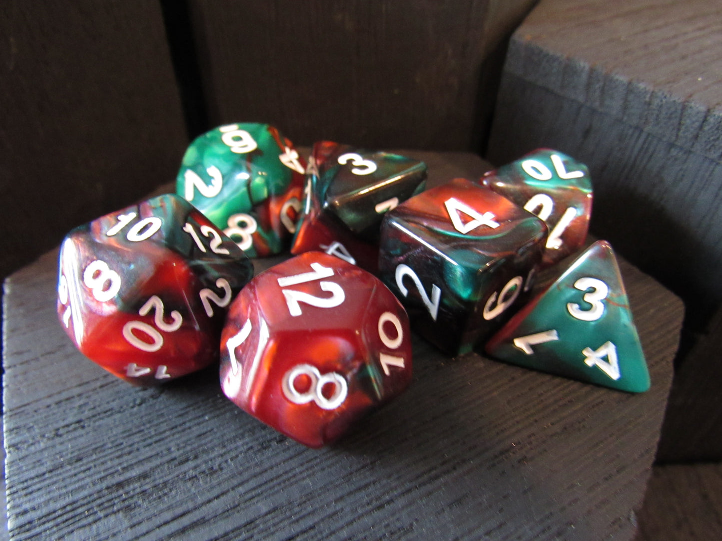 Set of polyhedral dice with red, green, and brown colors on a wooden surface.