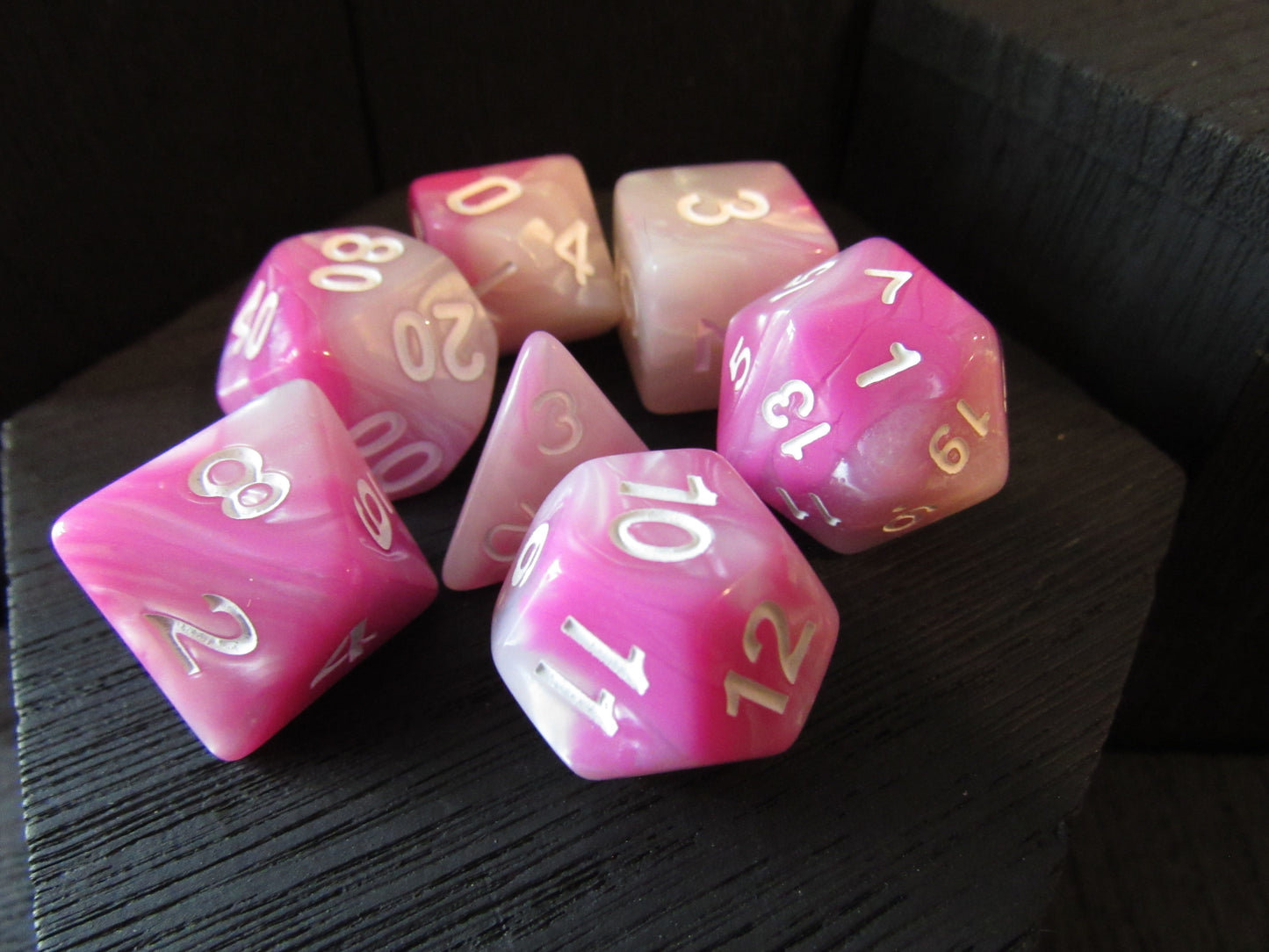Pink and white polyhedral dice set on a dark surface