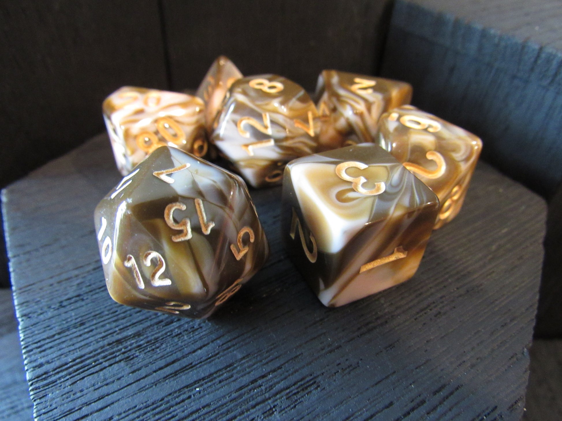 Set of polyhedral dice with gold and brown marbled pattern on a dark surface
