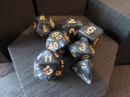 Set of black polyhedral dice with gold numbers on a wooden surface