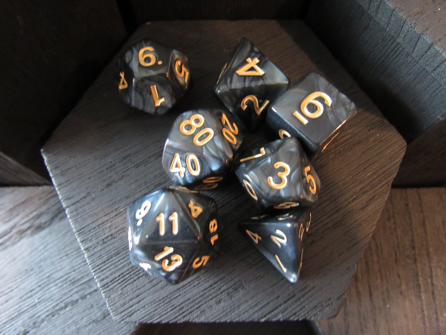 Set of black polyhedral dice with gold numbers on a wooden surface