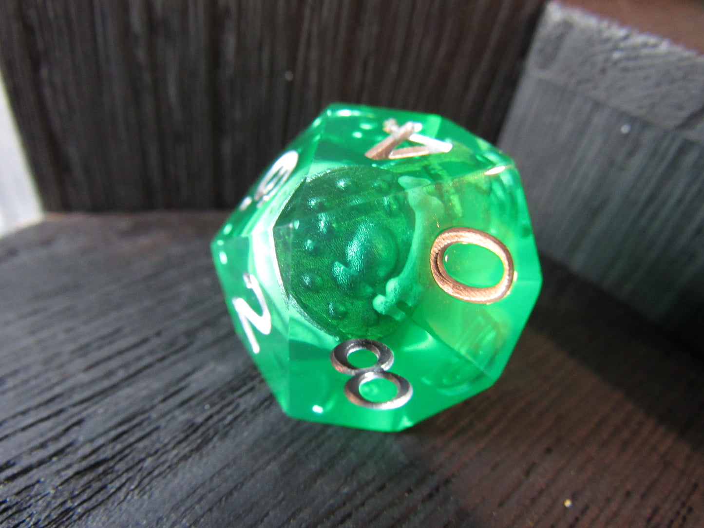 Green polyhedral dice with white numbers on a dark wooden surface gelatinous cube