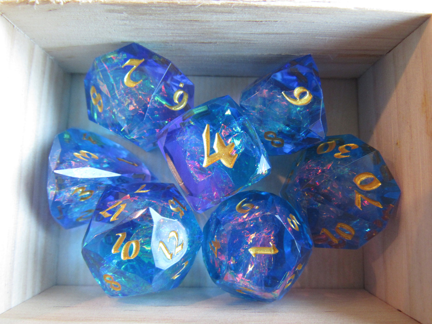 Set of blue and purple polyhedral dice with gold numbers in a wooden box. gem gemstone cut faceted resin dice