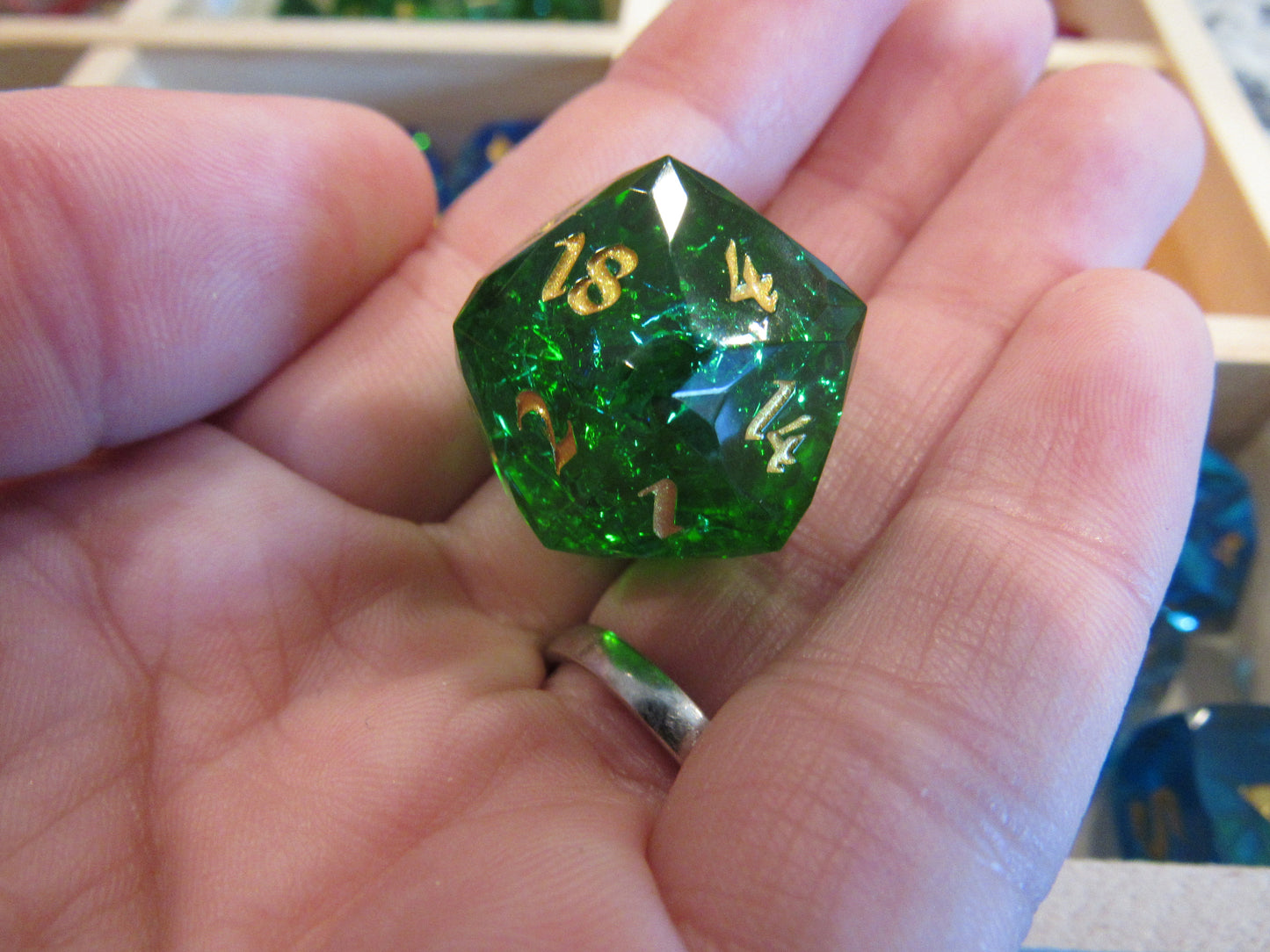 Green polyhedral die held in a hand with a blurred background gem gemstone crystal cut faceted resin dice