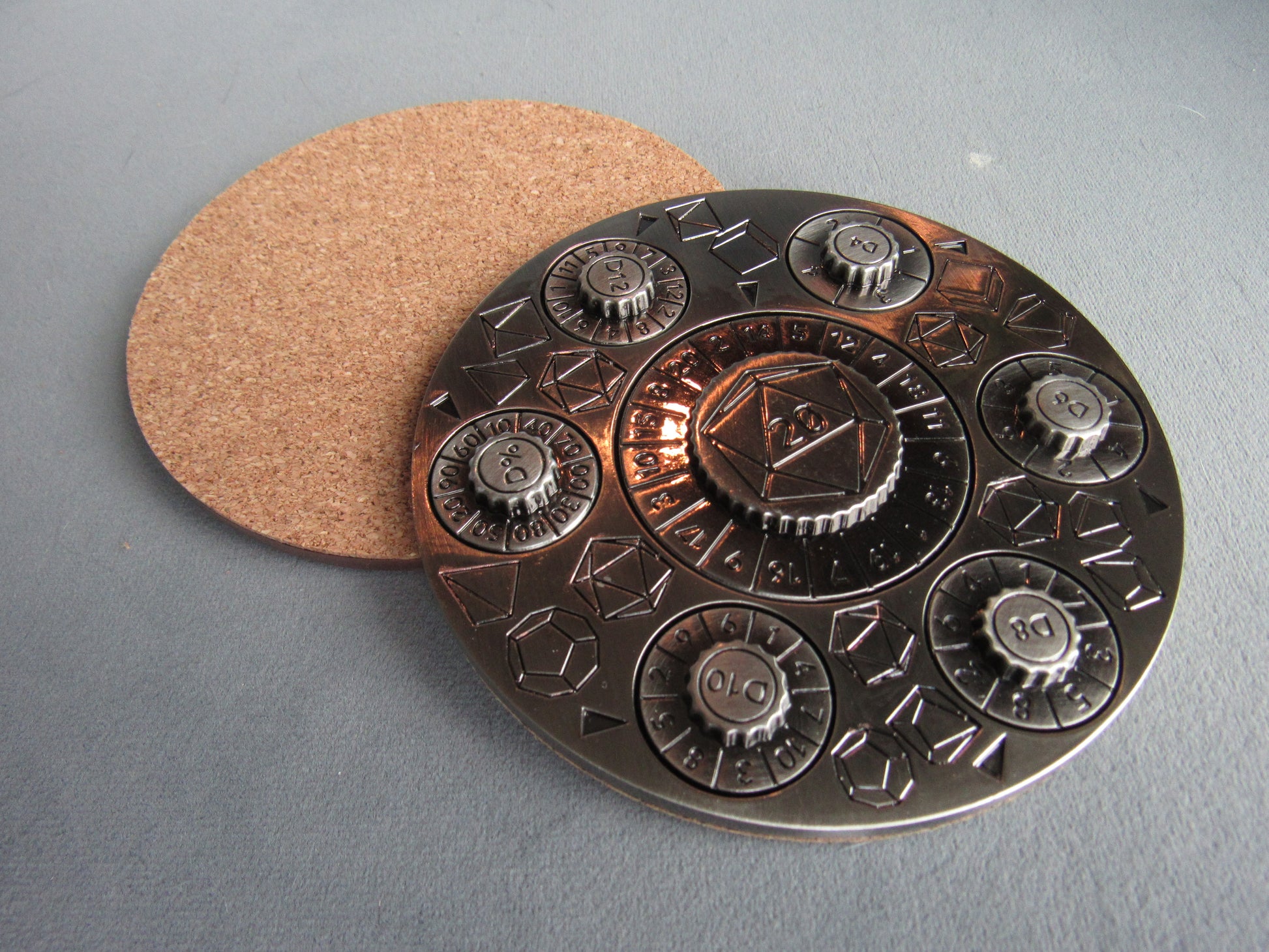 Decorative metal coaster with cork back on a gray surface dungeons and dragons spinner dice