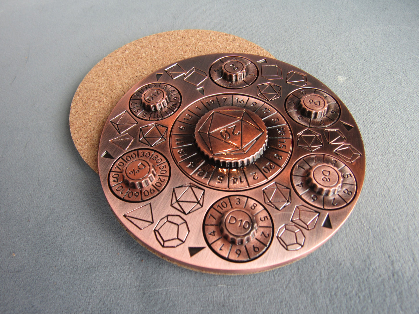 Copper-colored circular object with geometric designs on a gray surface dungeons and dragons spinner dice